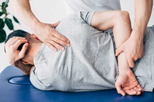 Person practicing gentle back mobility exercises beside a treatment table in a bright wellness room.